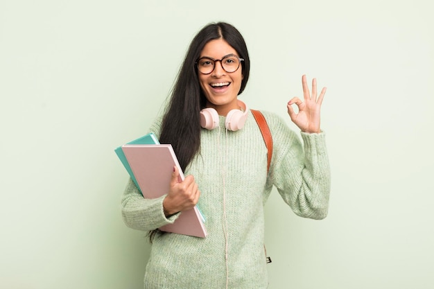 Joven mujer bonita hispana que se siente feliz mostrando aprobación con el concepto de estudiante de gesto bien