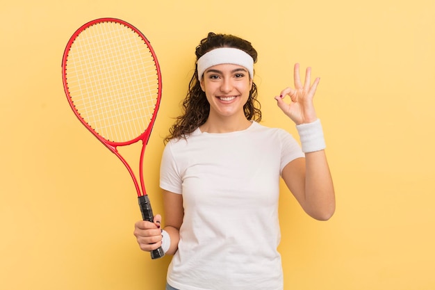 Joven mujer bonita hispana que se siente feliz mostrando aprobación con el concepto de tenis de gesto bien