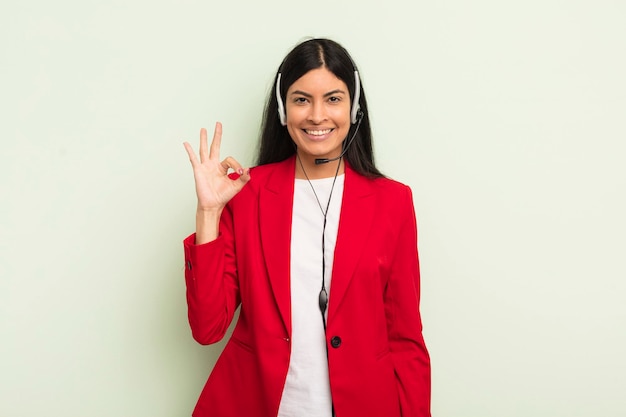 Joven mujer bonita hispana que se siente feliz mostrando aprobación con gesto bien concpet de telemarteker