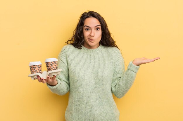 Joven mujer bonita hispana que se siente perpleja y confundida y dudando del concepto de café para llevar