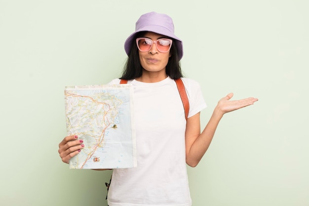 Foto joven mujer bonita hispana que se siente perpleja y confundida y que duda del concepto turístico y del mapa