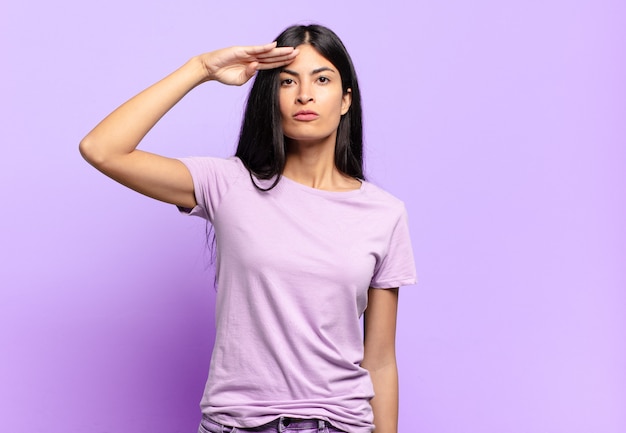 Joven mujer bonita hispana saludando con un saludo militar en un acto de honor y patriotismo, mostrando respeto