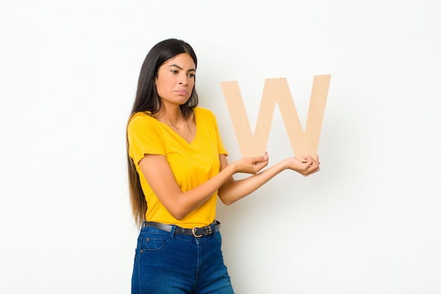 Foto joven mujer bonita latina triste, deprimida, infeliz, sosteniendo la letra w del alfabeto para formar una palabra o una oración.