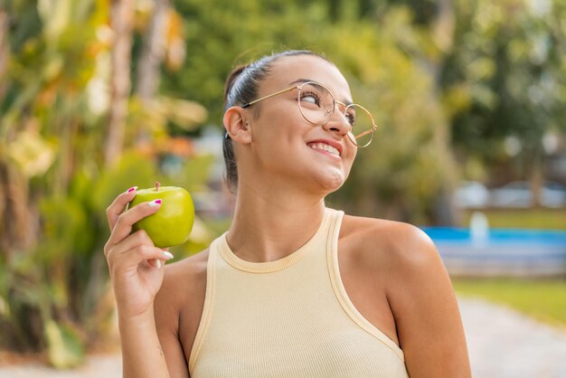 Foto joven mujer bonita con una manzana al aire libre mirando hacia arriba mientras sonríe