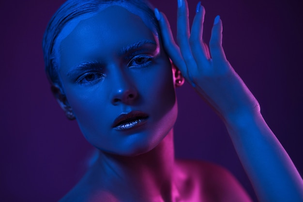 Joven mujer bonita con maquillaje fresco. Luces de neón azul y púrpura en la cara.