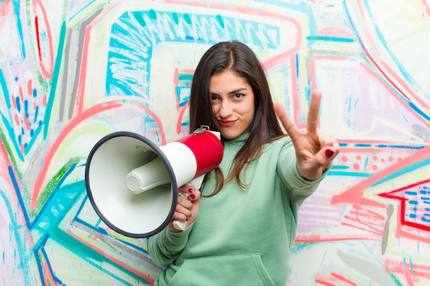 Joven mujer bonita con un megáfono contra la pared de graffiti