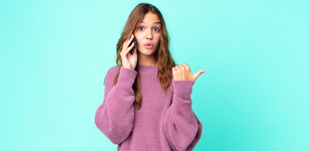 Joven mujer bonita mirando asombrado con incredulidad y usando un teléfono inteligente