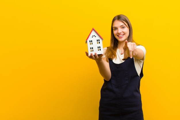 Joven mujer bonita con un modelo de casa sobre fondo naranja