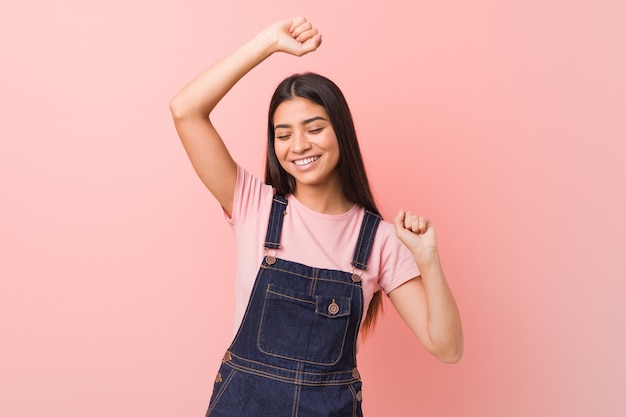 Joven mujer bonita con un mono de jeans celebrando un día especial, salta y levanta los brazos con energía