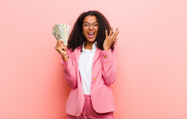 Joven mujer bonita negra con billetes de dólar contra la pared rosa