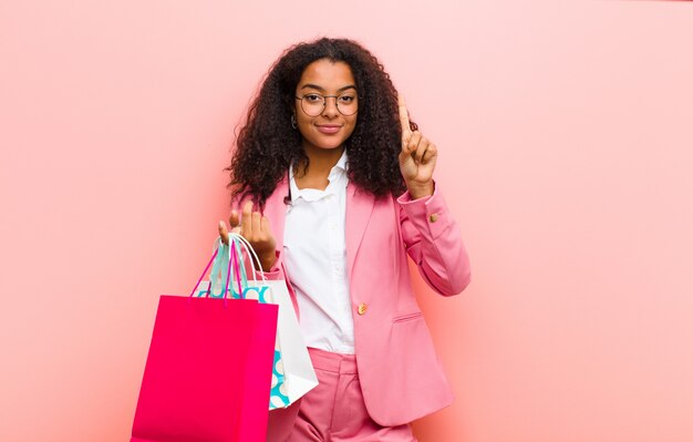 Joven mujer bonita negra con bolsas de compras contra la pared rosa