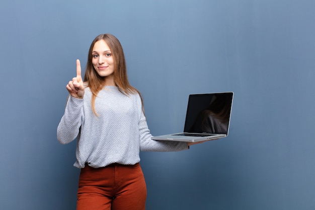 Joven mujer bonita con una pared azul portátil con un copyspace