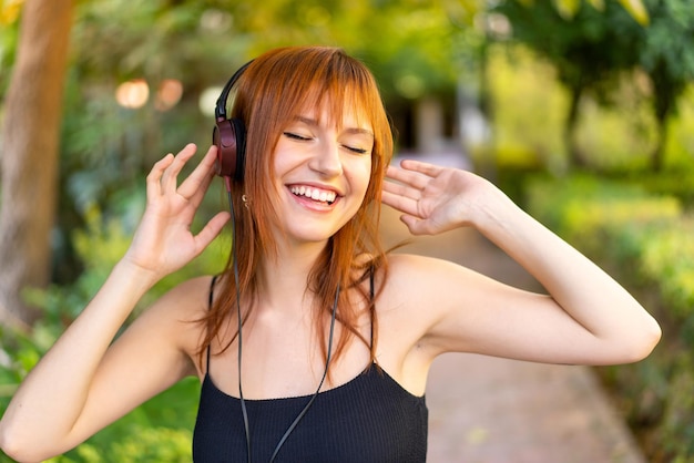 Joven mujer bonita pelirroja al aire libre escuchando música y cantando