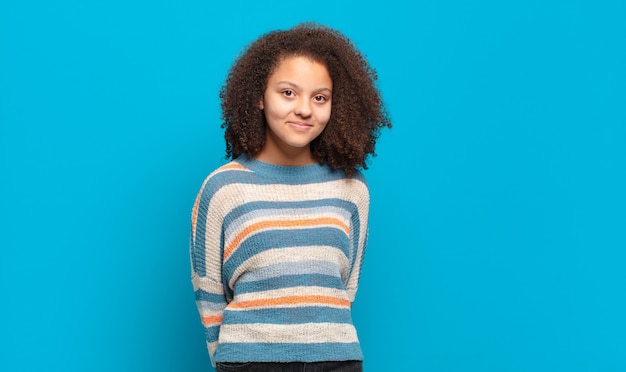 Joven mujer bonita con pelo afro y suéter a rayas posando en la pared azul