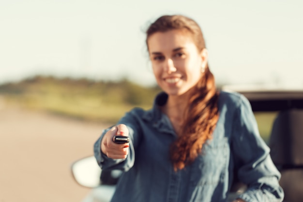 Joven mujer bonita de pie cerca de convertible con llaves en mano