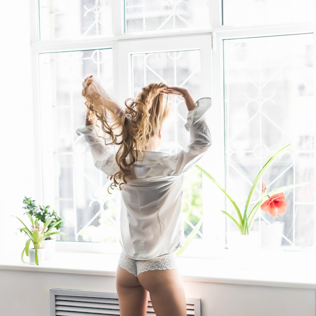 Foto joven mujer bonita de pie en la ventana abierta y mirando fuera goza de descanso