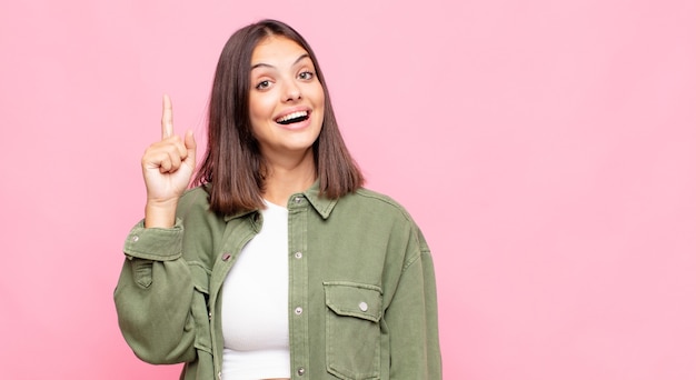 Joven mujer bonita que se siente como un genio feliz y emocionado después de realizar una idea, levantando alegremente el dedo, ¡eureka!