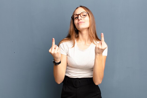 Joven mujer bonita que se siente provocativa, agresiva y obscena, moviendo el dedo medio, con una actitud rebelde contra el gris