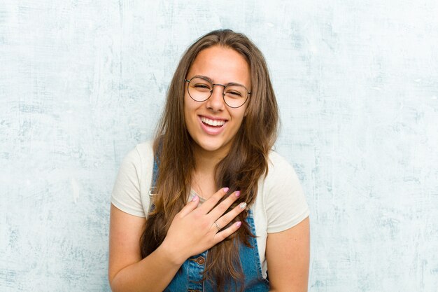 Joven mujer bonita riéndose a carcajadas de alguna broma hilarante, sintiéndose feliz y alegre, divirtiéndose contra la pared del grunge