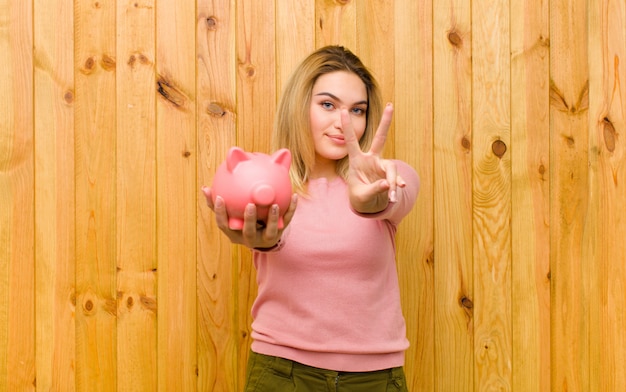 Foto joven mujer bonita rubia con una alcancía contra la pared de madera