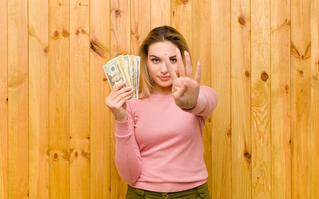 Joven mujer bonita rubia con billetes de dólar contra la madera