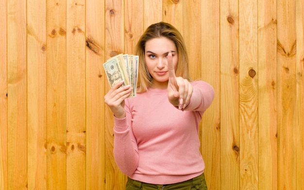 Foto joven mujer bonita rubia con billetes de dólar contra la pared de madera