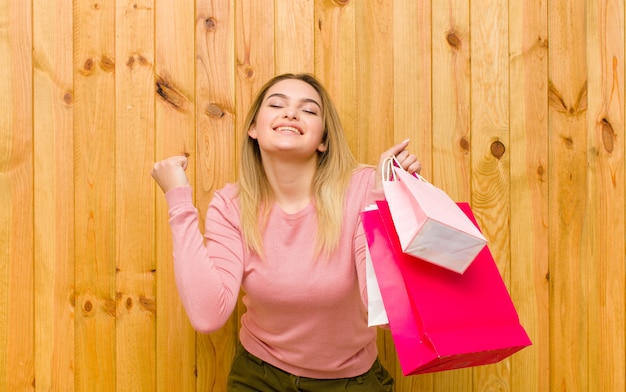 Joven mujer bonita rubia con bolsas de compras contra la pared de madera