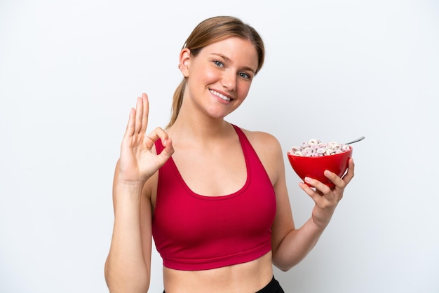 Joven mujer bonita rubia desayunando leche aislada de fondo blanco mostrando el signo de ok con los dedos