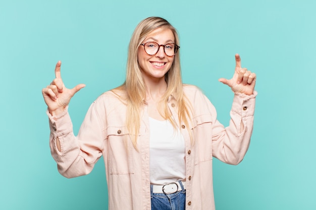 Joven mujer bonita rubia enmarcando o delineando su propia sonrisa con ambas manos, mirando positivo y feliz, concepto de bienestar