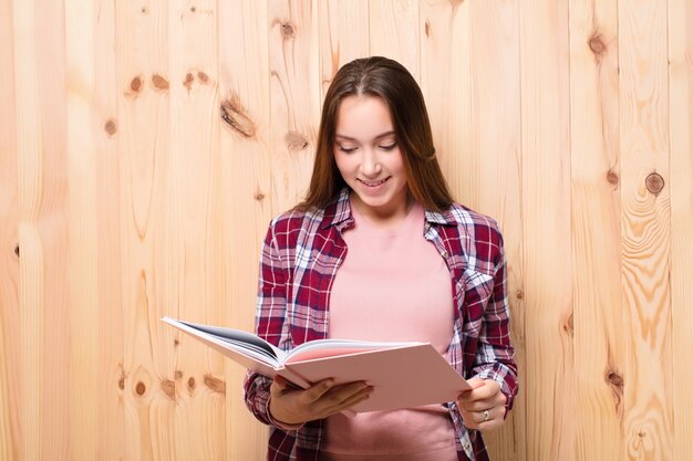 Joven mujer bonita rubia con un libro contra la pared de madera