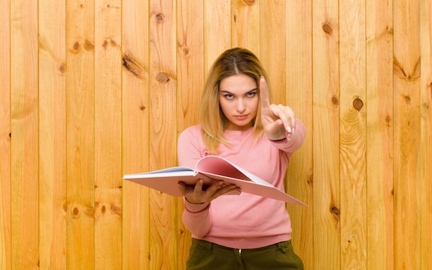 Foto joven mujer bonita rubia con libros contra la pared de madera