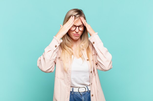 Joven mujer bonita rubia que parece estresada y frustrada, trabajando bajo presión con dolor de cabeza y preocupada por problemas