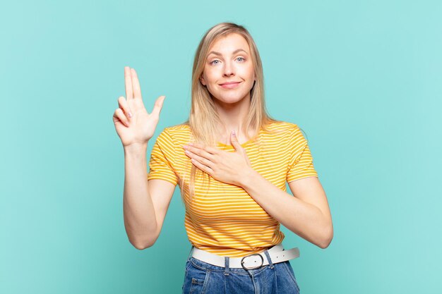 Foto joven mujer bonita rubia que parece feliz, segura y digna de confianza, sonriendo y mostrando el signo de la victoria, con una actitud positiva