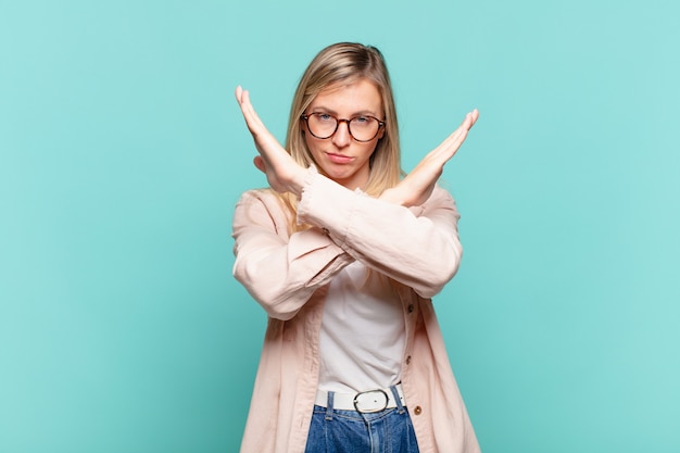 Joven mujer bonita rubia que parece molesta y harta de tu actitud, ¡diciendo basta! manos cruzadas al frente, diciéndote que te detengas