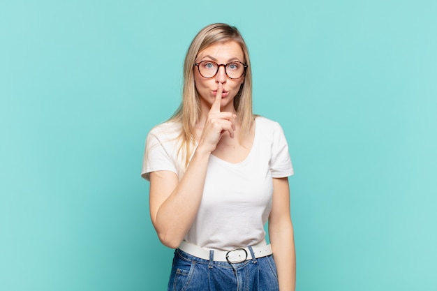 Joven mujer bonita rubia que parece seria y cruzada con el dedo presionado en los labios exigiendo silencio o silencio, manteniendo un secreto