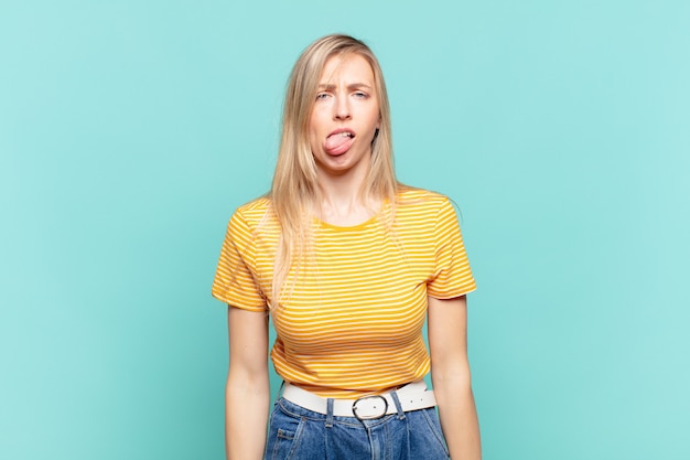 Joven mujer bonita rubia que se siente disgustada e irritada, sacando la lengua, disgustando algo desagradable y asqueroso