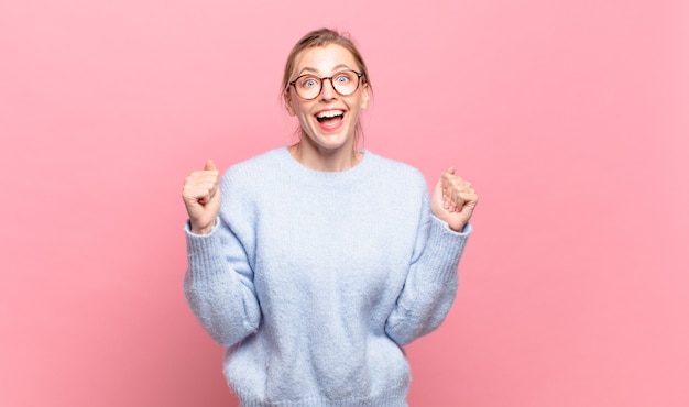 Joven mujer bonita rubia que se siente sorprendida, emocionada y feliz, riendo y celebrando el éxito, diciendo ¡guau!