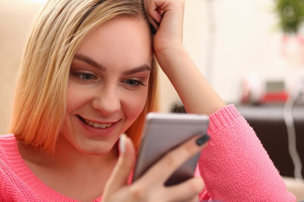 Joven mujer bonita rubia sentada en el sofá mantenga el teléfono inteligente en las manos charlar con amigos