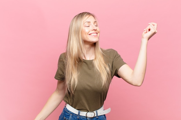 Joven mujer bonita rubia sonriendo, sintiéndose despreocupada, relajada y feliz, bailando y escuchando música, divirtiéndose en una fiesta