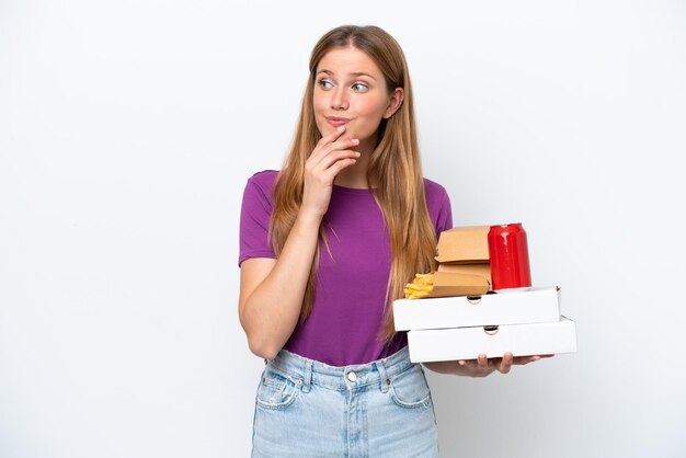 Joven mujer bonita rubia sosteniendo comida rápida aislada de fondo blanco mirando hacia arriba mientras sonríe