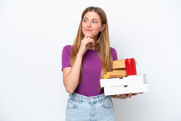 Joven mujer bonita rubia sosteniendo comida rápida aislada de fondo blanco y mirando hacia arriba