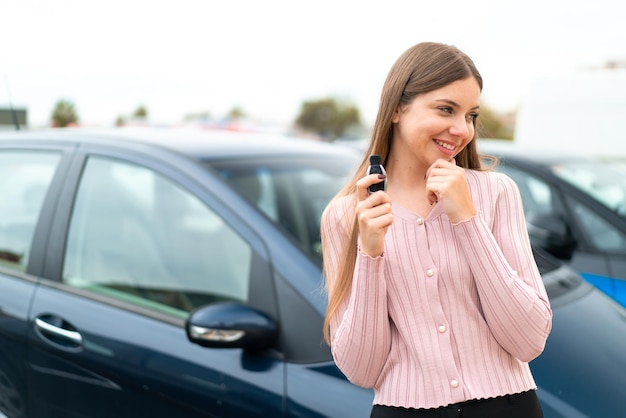 Joven mujer bonita rubia sosteniendo las llaves del auto al aire libre pensando en una idea y mirando hacia el lado