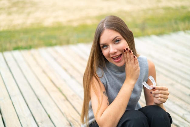 Joven mujer bonita rubia sosteniendo llaves invisibles al aire libre susurrando algo