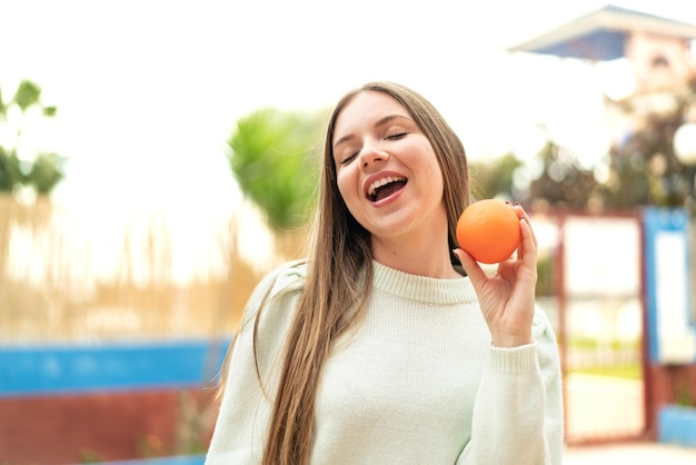 Joven mujer bonita rubia sosteniendo una naranja con expresión feliz