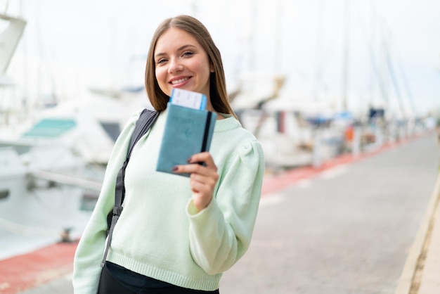 Joven mujer bonita rubia sosteniendo un pasaporte al aire libre con expresión feliz