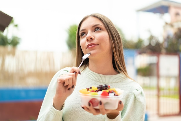 Joven mujer bonita rubia sosteniendo un plato de fruta al aire libre