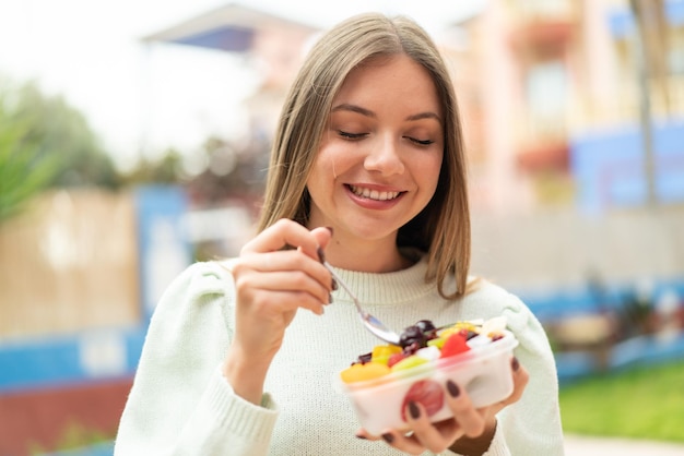 Joven mujer bonita rubia sosteniendo un plato de fruta al aire libre