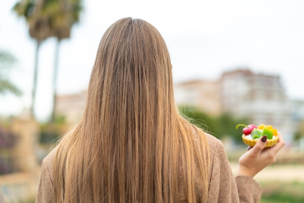 Joven mujer bonita rubia sosteniendo una tartaleta al aire libre en posición trasera