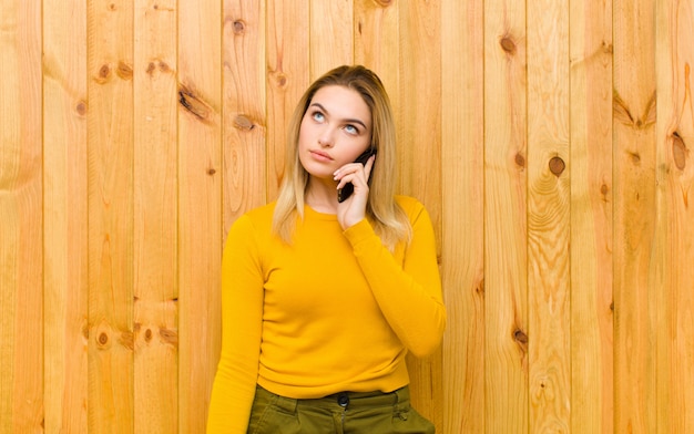 Joven mujer bonita rubia con un teléfono móvil contra la pared de madera