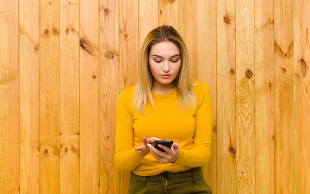 Joven mujer bonita rubia con un teléfono móvil contra la pared de madera